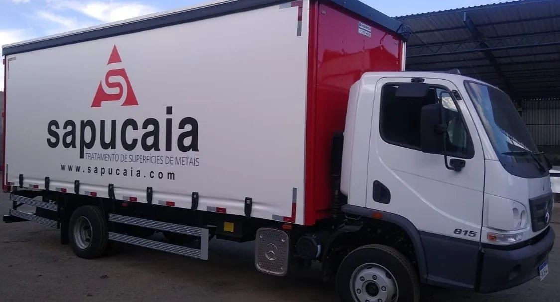 Caminhão baú branco e vermelho com a marca Sapucaia, o descritivo “Tratamento de superfícies de metais” e o endereço www.sapucaia.com