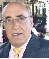 Retrato de homem de terno escuro, óculos e gravata amarela