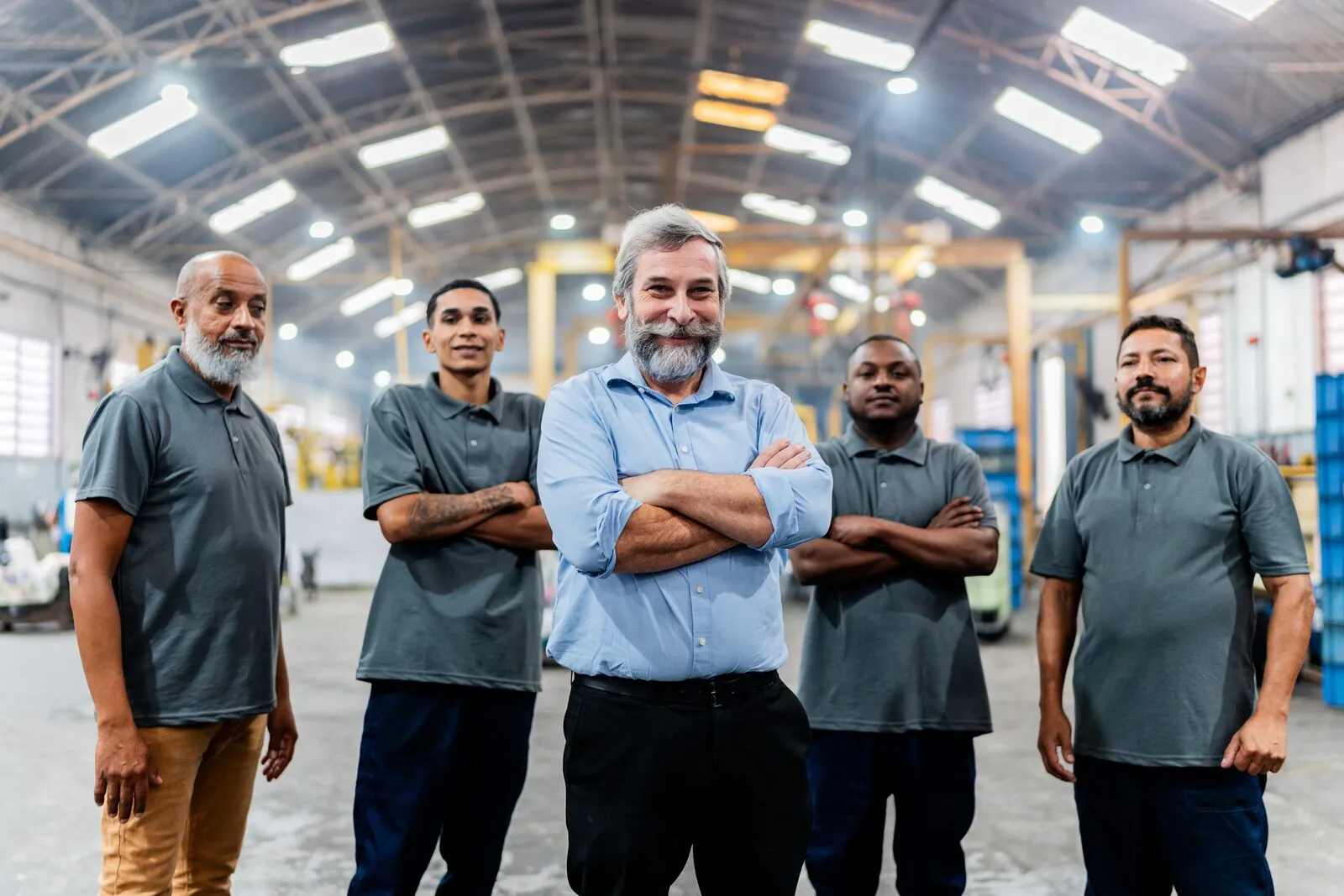 Cinco integrantes da equipe da Sapucaia enfileirados no piso de fábrica