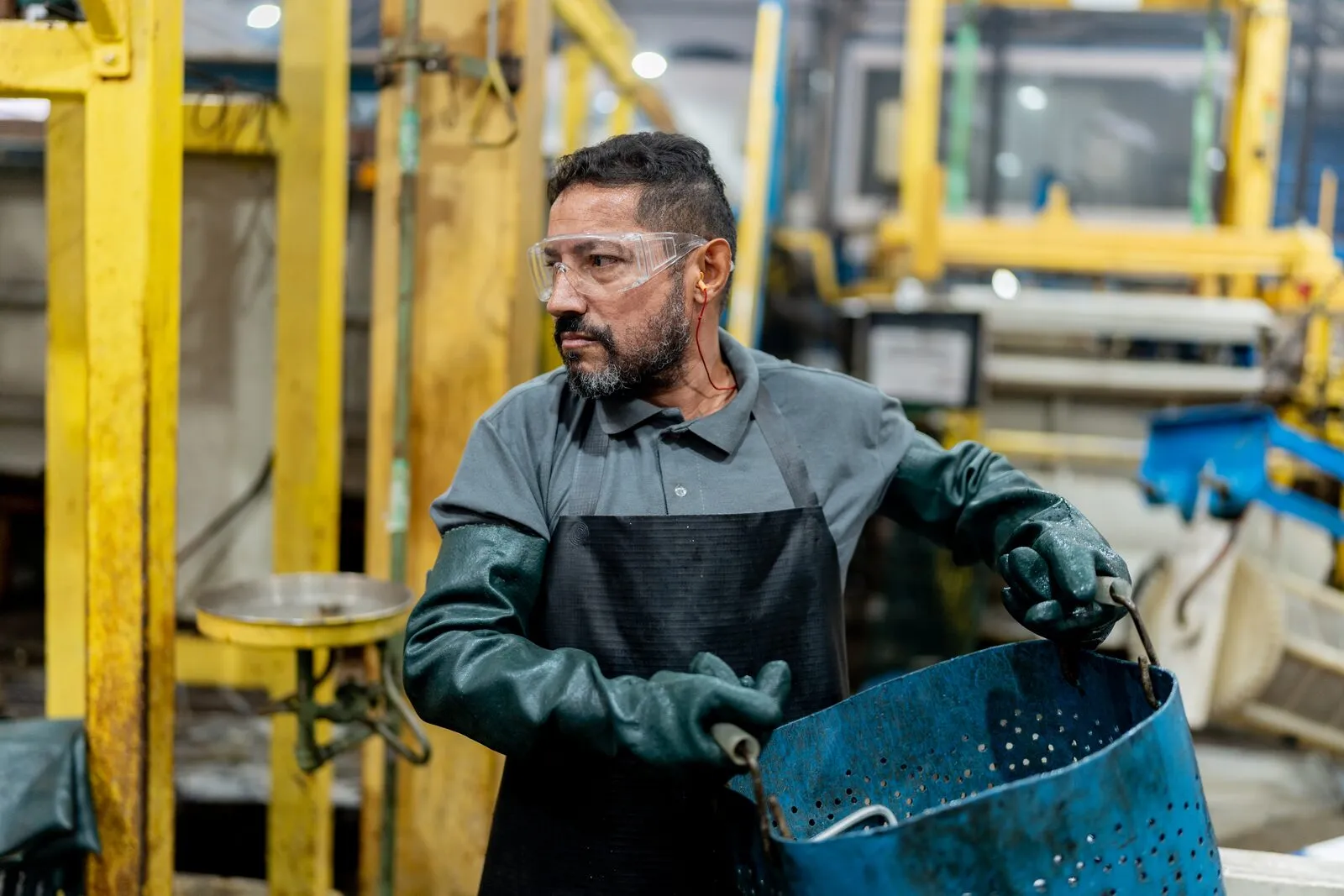Operador carregando cesto de peças entre os tanques da linha
