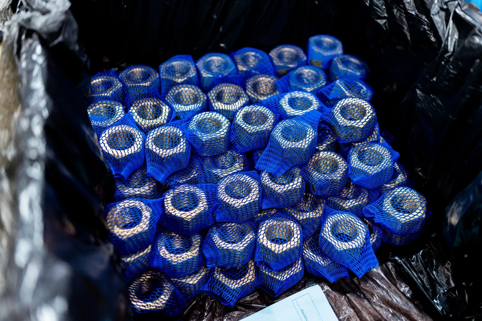 Porcas sextavadas grandes, cada uma em malha azul de proteção, acondicionadas em caixa forrada para embarque