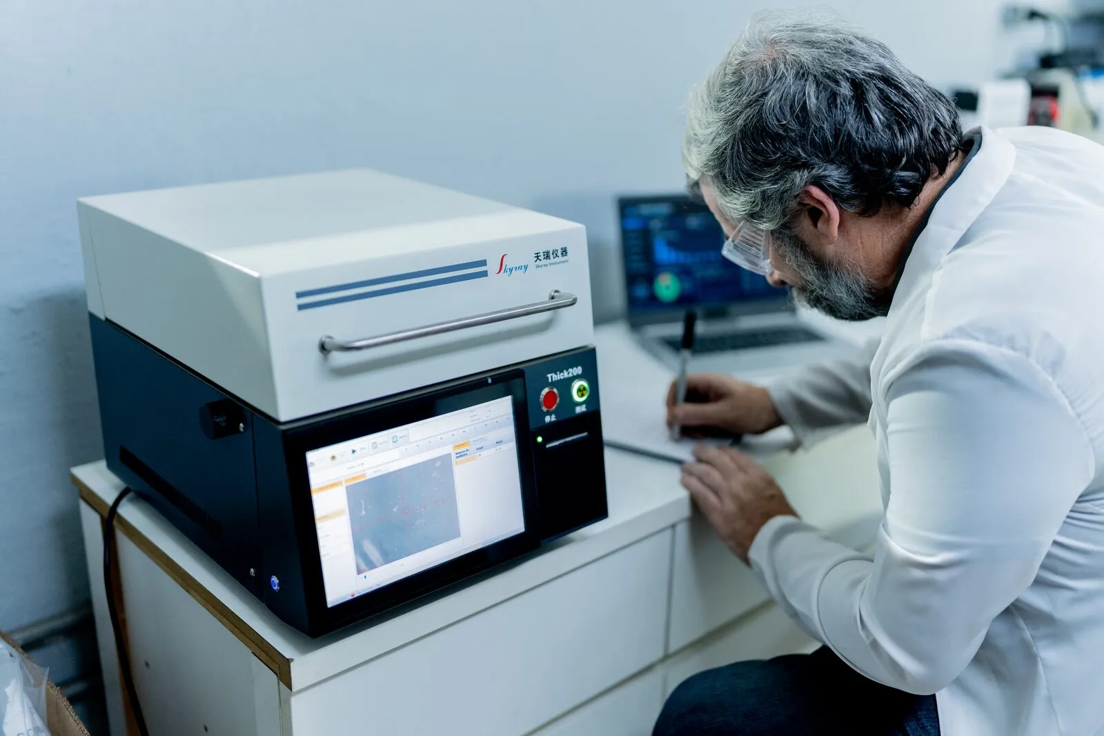 Analista de bata branca operando o espectrômetro de fluorescência de raios X na bancada do laboratório