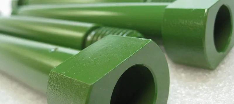 Estojos e porcas alongadas com revestimento verde fosco e uniforme, em enquadramento fechado sobre a rosca