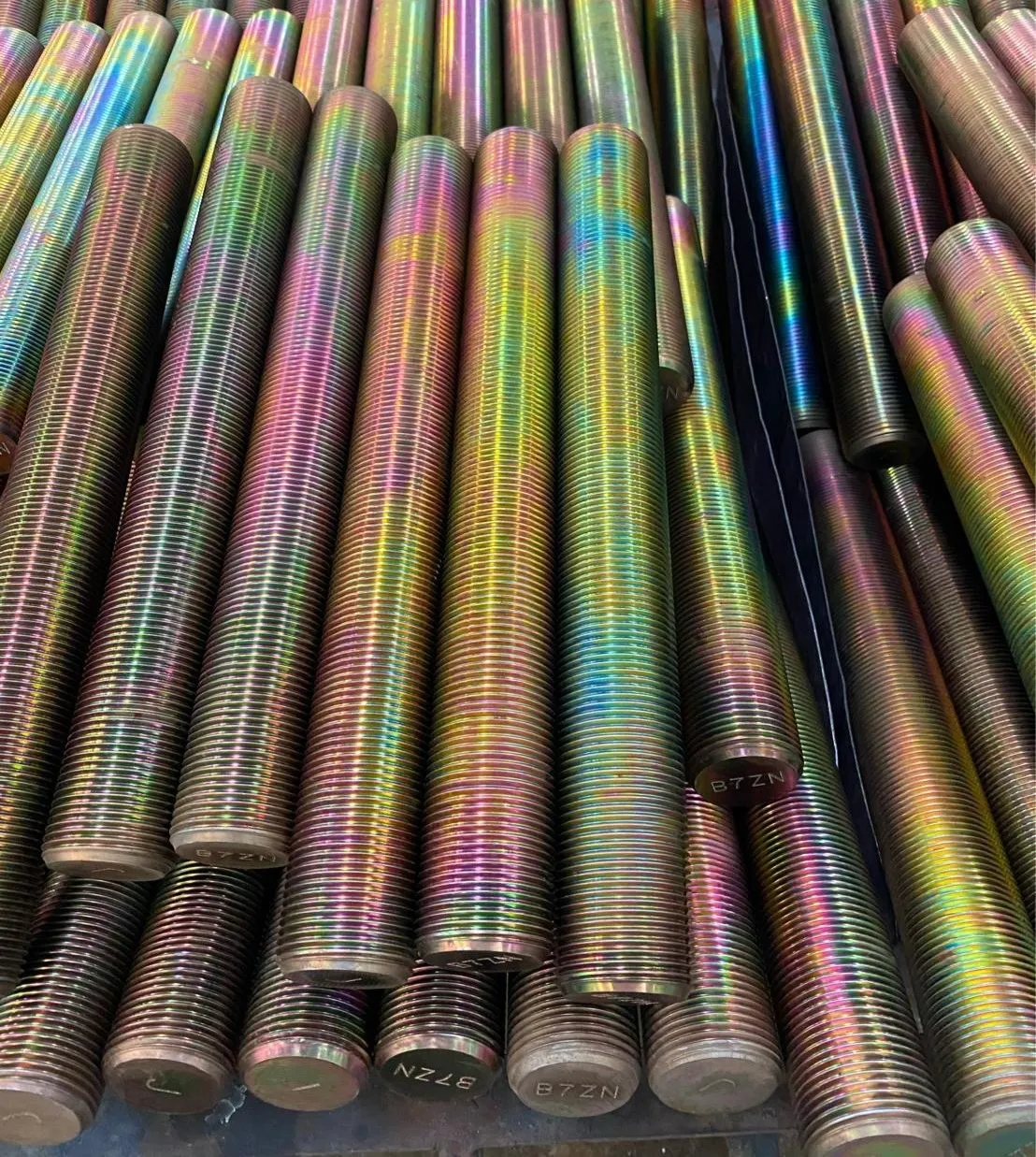 Estojos roscados alinhados lado a lado, com a marcação B7ZN gravada no topo de cada um, em acabamento iridescente que varia do verde ao rosa